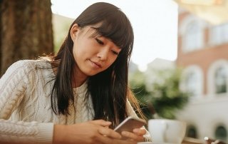 Chinese woman typing text message on smart phone in a cafe. Image of young woman sitting at a table with a coffee using mobile phone.