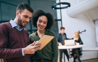 Coworkers standing in an office, looking at a digital tablet