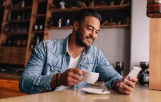 Handsome young man having coffee and using mobile phone