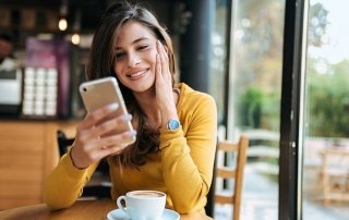 Young smiling woman using smarphone in the cafe. Front view.