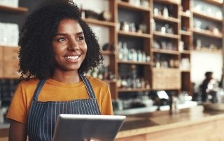 Young female owner holding digital tablet in her cafe looking aw