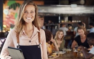 Portrait Of Waitress Holding Menus Serving In Busy Bar Restaurant