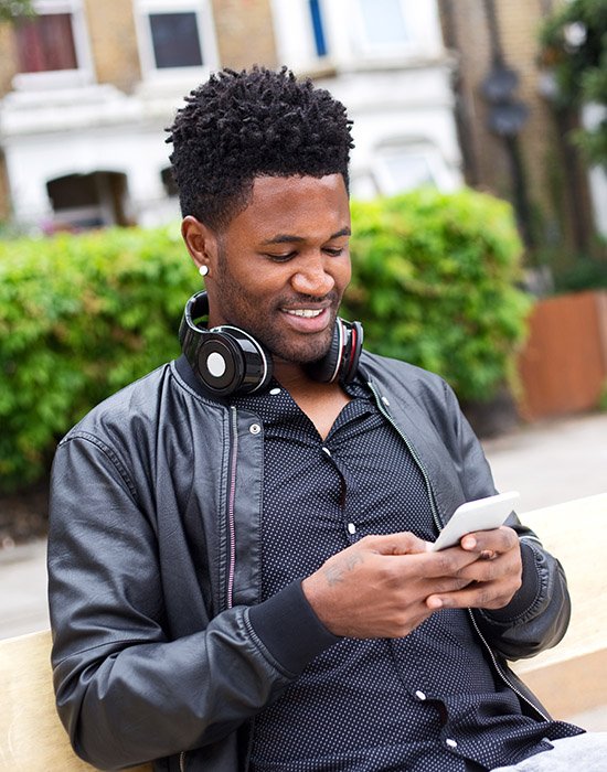 young man reading his text messages sat on a bench in the street